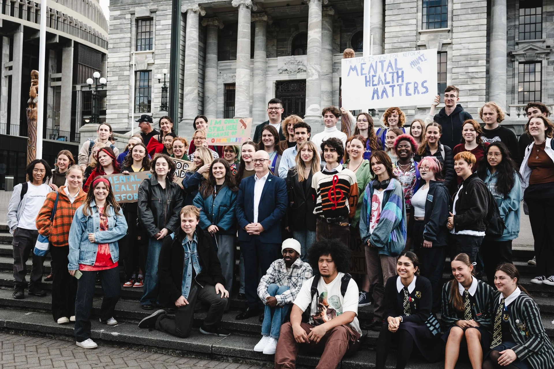 MHMI rangatahi gathered on the steps of Parliament with a hand-painted Mental Health Matters sign
